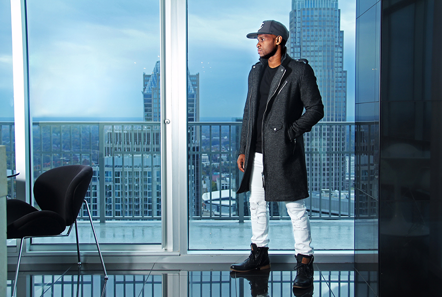 Oliver Crooms stands in a studio with the skyline of Charlotte behind him