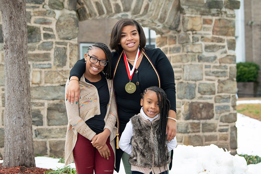 Courtney Johnson stands with her daughters near the archway on campus.