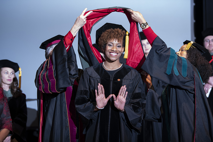 student forms a W with her hands as she receives her doctoral hood 