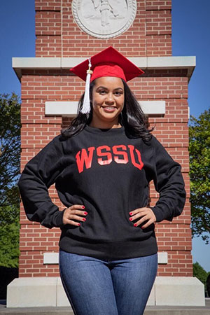 Amber Romero stands in front of the clocktower with WSSU sweatshirt and graduation cap
