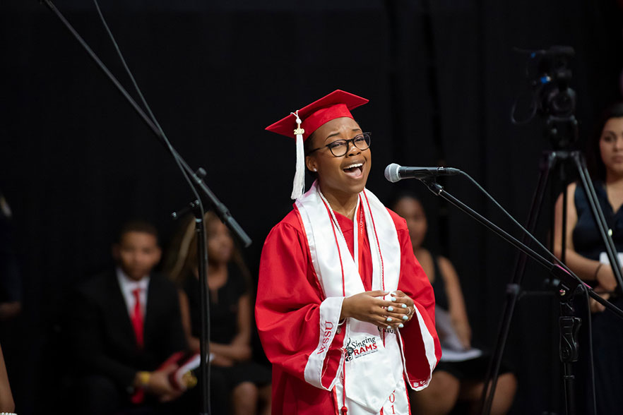 Nia Lewis in her graduation cap and gown, stands behind a microphone