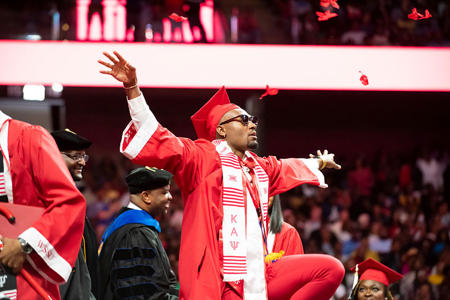 Graduate in cap and gown and sunglasses tosses red rose petals into the air