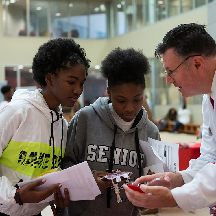 Students look at petri dish held by teacher