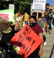 Hispanic girl wearing burgundy shirt holding up a red poster with black letters that reads "No Money, No Rent!"
